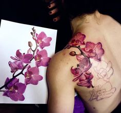 a woman with tattoos on her back holding up a piece of paper that has orchids painted on it