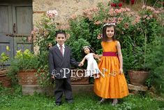 two children dressed up in formal wear standing next to each other with their hands on the doll