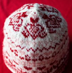 a red and white knitted hat sitting on top of a red cloth covered table