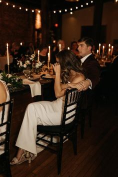 a man and woman sitting at a dinner table with candles in the background as they look into each other's eyes