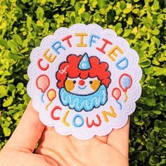 someone holding up a patch with the words certified clown on it in front of some bushes