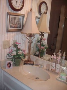 a white sink sitting under a mirror next to a lamp and pictures on the wall