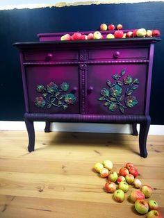 an old dresser has apples on it and is purple with green leaves painted on the drawers