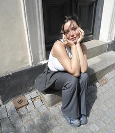 a woman sitting on the ground in front of a door with her hands to her face