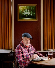 an older man sitting at a table with a glass of beer