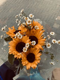 a vase filled with lots of sunflowers on top of a glass table next to a brick sidewalk