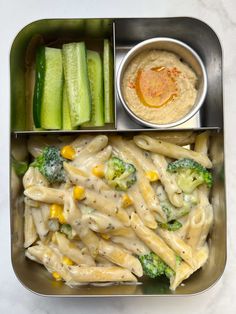 a metal container filled with pasta and veggies next to dipping sauce in a bowl