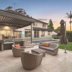 an outdoor living area with couches, tables and umbrellas next to a swimming pool