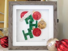 a frame with some christmas decorations in it on a shelf next to ornaments and a red ornament