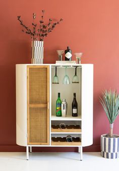 a cabinet with wine glasses and bottles on it in front of a wall painted pink