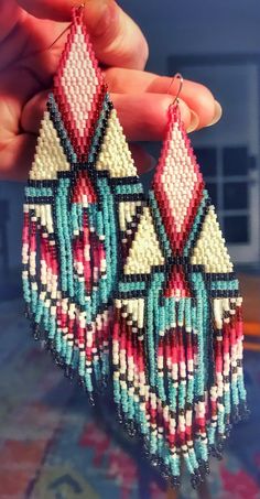 a pair of colorful beaded earrings hanging from a persons hand