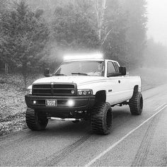 the truck is driving down the road with its lights on and foggy trees in the background