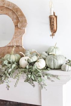 white pumpkins and greenery sit on a mantel in front of a mirror