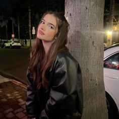 a woman standing next to a tree in front of a white car