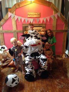 children posing for a photo in front of a toy cow with other toys on the floor