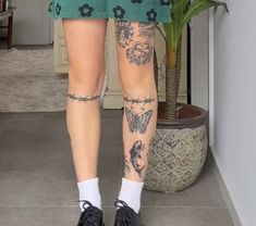 a woman with tattoos on her legs standing next to a potted plant