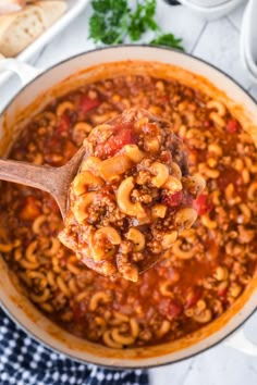 a ladle full of chili macaroni and cheese being held by a wooden spoon