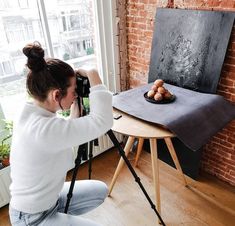 a woman taking a photo of some food on a table in front of a window