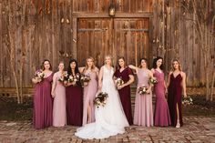 a group of women standing next to each other in front of a wooden building holding bouquets