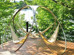 an outdoor swing chair on a wooden deck with trees and water in the back ground