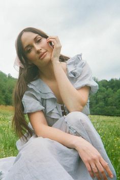 a woman sitting in the grass talking on a cell phone with her hand to her ear