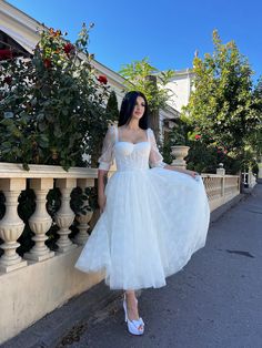 a woman in a white dress is standing on the side of a building with her hands on her hips