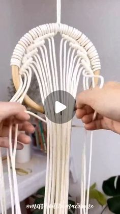 two hands are holding yarn in front of a white hanging object with strings attached to it