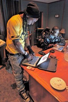 a man with dreadlocks using a laptop on a desk in front of two other men