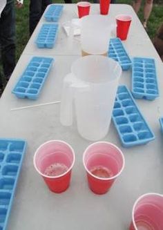 plastic cups are lined up on a long table with ice trays and red cups