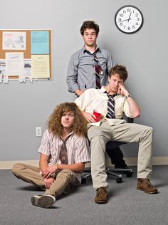 three young men sitting in an office with a clock on the wall