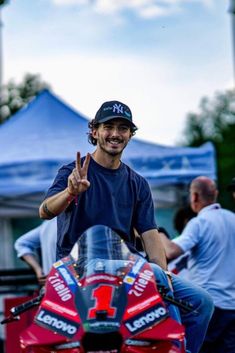 a man sitting on top of a red motorcycle giving the peace sign with his hand