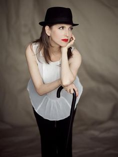 a woman in white shirt and black hat holding an umbrella with her hand on the handle