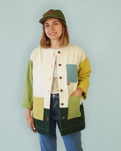 a woman standing in front of a blue wall wearing a green hat and cardigan