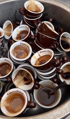 coffee cups filled with different types of saucers and spoons in a metal bowl