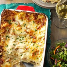 a casserole dish with meat and cheese on it next to a bowl of salad