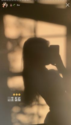 the silhouette of a woman taking a photo with her cell phone while standing in front of a window