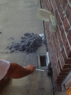 a person standing next to a brick building near a hole in the ground with something on it