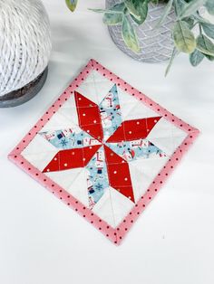 a red and white quilted star sitting on top of a table next to a potted plant