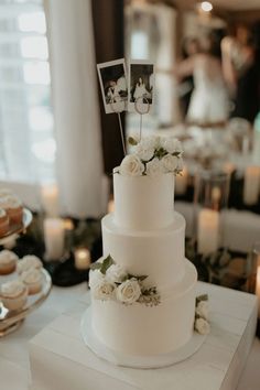 a white wedding cake with flowers and photos on the top is sitting on a table