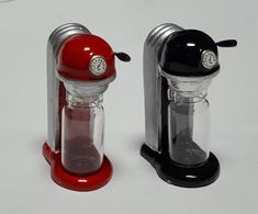 two miniature coffee grinders sitting side by side on a white surface, one red and the other black