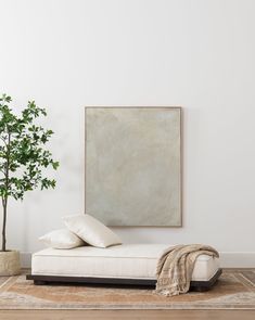 a white couch sitting in front of a painting on the wall next to a potted plant