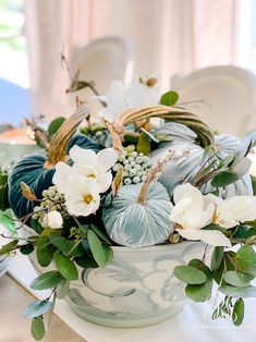 a bowl filled with flowers and greenery on top of a white table cloth covered table