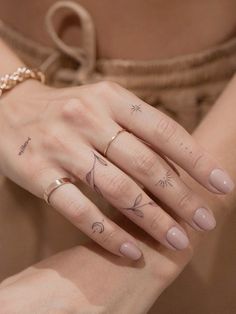 a woman's hand with three different tattoos on her fingers and two other rings