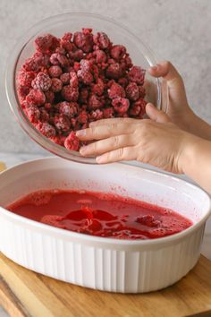 a person holding a bowl full of raspberries in front of a red liquid