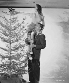 black and white photograph of a man holding a young boy in front of a christmas tree