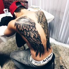 a man sitting on the ground with his back turned to the camera and an eagle tattoo on his upper half