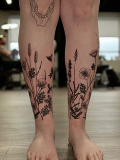 a woman's legs with flowers and a skull tattoo on them, while standing in a room