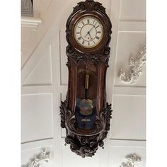 an ornate wooden clock mounted to the side of a white wall next to a stair case