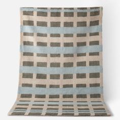 a gray and blue blanket with squares on it, sitting against a white wall in the background