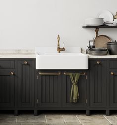 a kitchen with black cabinets and white counter tops, gold pulls on the faucet